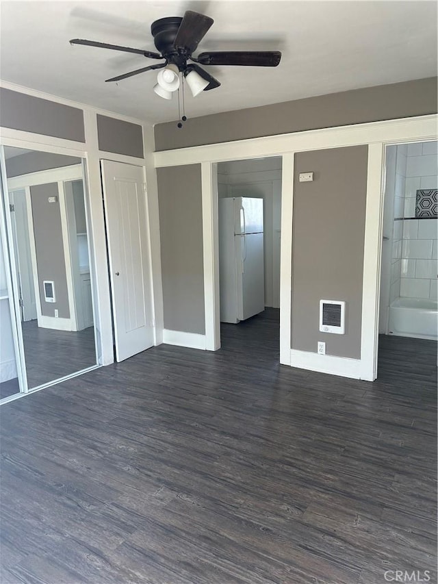 unfurnished bedroom with dark wood-type flooring, ceiling fan, white refrigerator, and heating unit