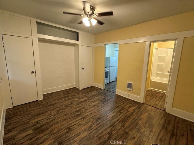 unfurnished bedroom featuring ceiling fan, dark wood-type flooring, white refrigerator, and ensuite bathroom