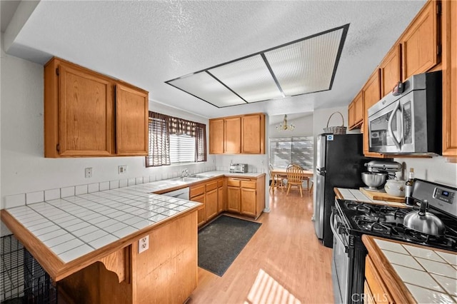 kitchen with tile countertops, kitchen peninsula, appliances with stainless steel finishes, light wood-type flooring, and a textured ceiling