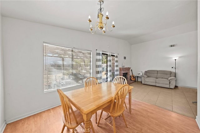 dining space featuring light wood-type flooring, vaulted ceiling, a brick fireplace, and an inviting chandelier