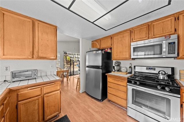 kitchen with stainless steel appliances, tile countertops, and light hardwood / wood-style flooring