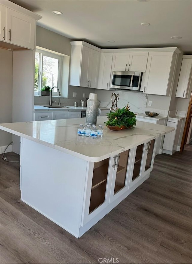 kitchen featuring white cabinets, a center island, dark hardwood / wood-style flooring, sink, and light stone counters