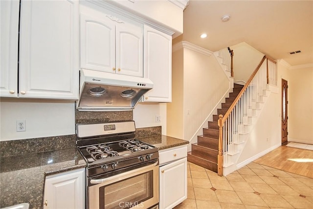 kitchen with dark stone countertops, stainless steel gas stove, white cabinets, and ornamental molding