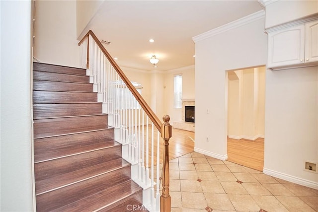 stairs with tile patterned floors, ornamental molding, and a fireplace