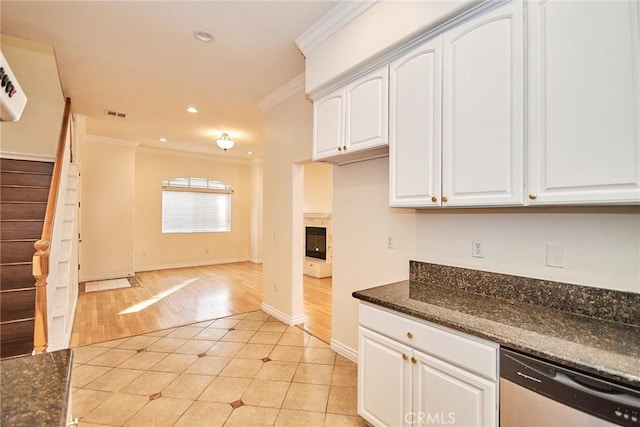 kitchen featuring white cabinetry, stainless steel dishwasher, dark stone countertops, a fireplace, and light tile patterned floors