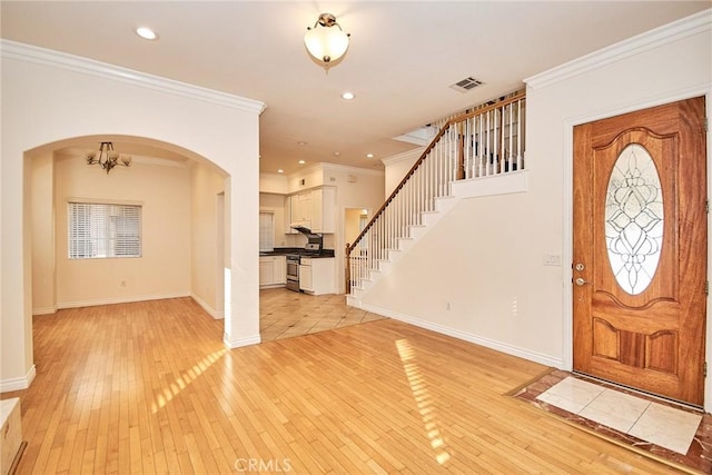 entryway featuring light wood-type flooring, ornamental molding, and a chandelier