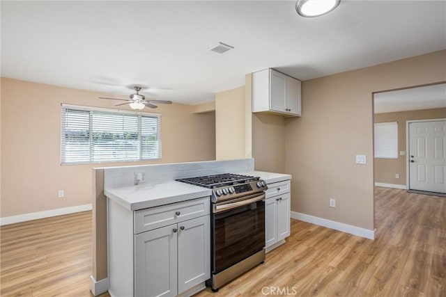 kitchen featuring ceiling fan, stainless steel gas range oven, white cabinetry, and light hardwood / wood-style floors