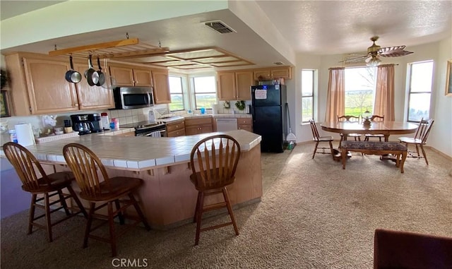 kitchen with kitchen peninsula, a breakfast bar area, stainless steel appliances, ceiling fan, and light brown cabinets