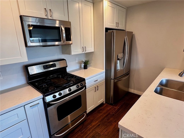 kitchen with appliances with stainless steel finishes, dark wood-type flooring, white cabinetry, sink, and light stone counters