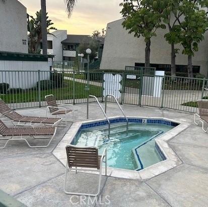 pool at dusk with a hot tub and a patio