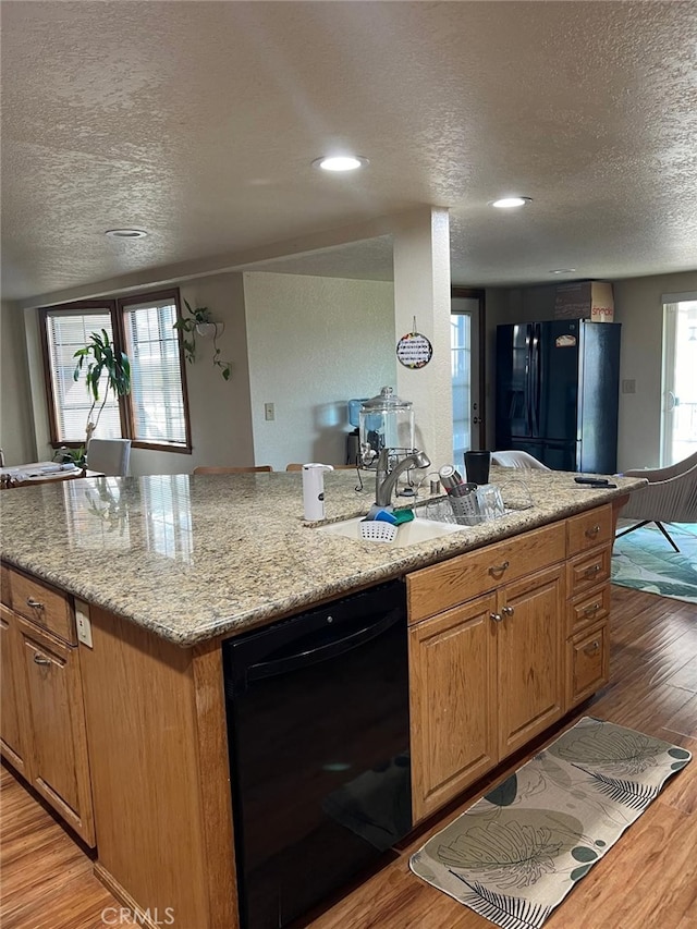 kitchen with light wood-style flooring, a sink, a textured ceiling, light stone countertops, and black appliances