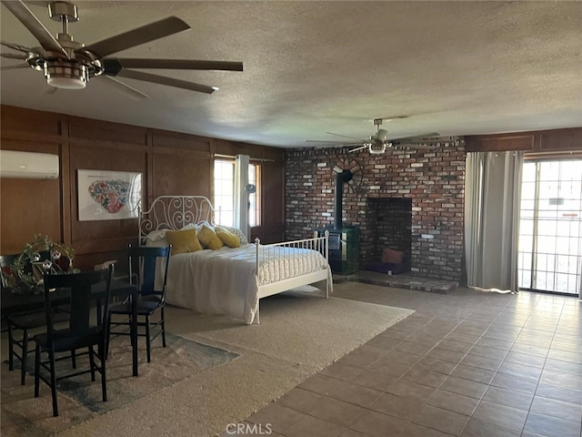 bedroom featuring a ceiling fan, a wall unit AC, a wood stove, a textured ceiling, and wood walls