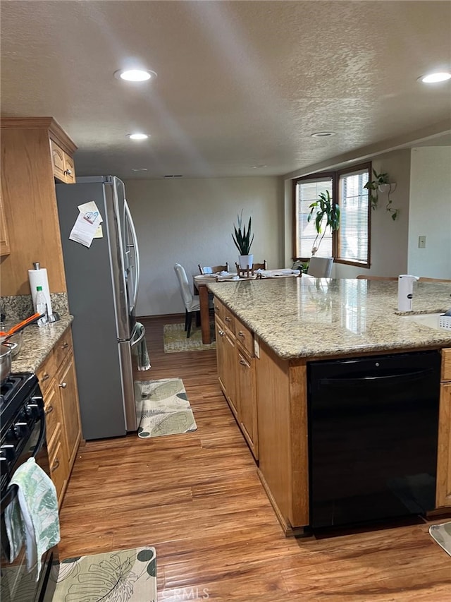 kitchen featuring recessed lighting, light wood-style floors, a kitchen island, light stone countertops, and black appliances