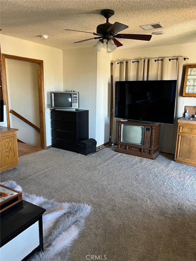 living area featuring ceiling fan, visible vents, a textured ceiling, and carpet flooring