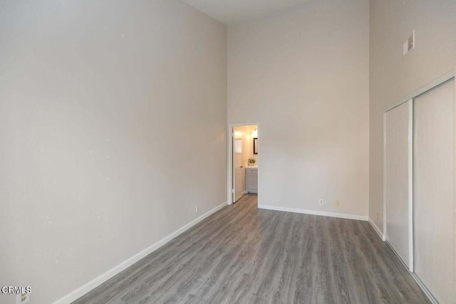 unfurnished bedroom featuring ensuite bath, a closet, a towering ceiling, and dark wood-type flooring