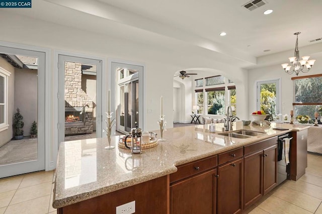 kitchen with ceiling fan with notable chandelier, sink, light stone countertops, and an island with sink