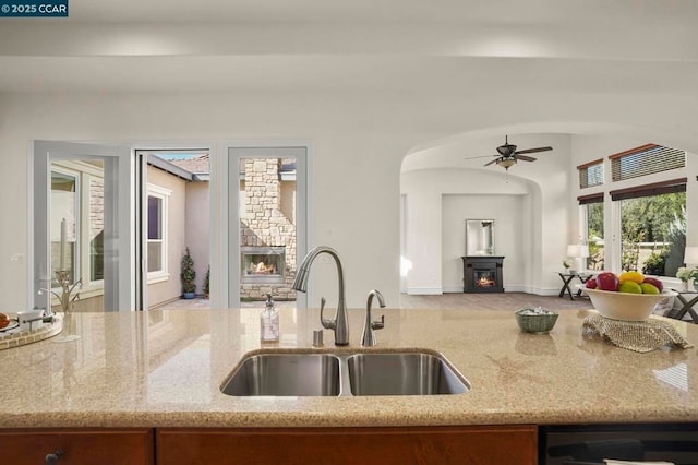 kitchen featuring light stone countertops, sink, black dishwasher, and ceiling fan