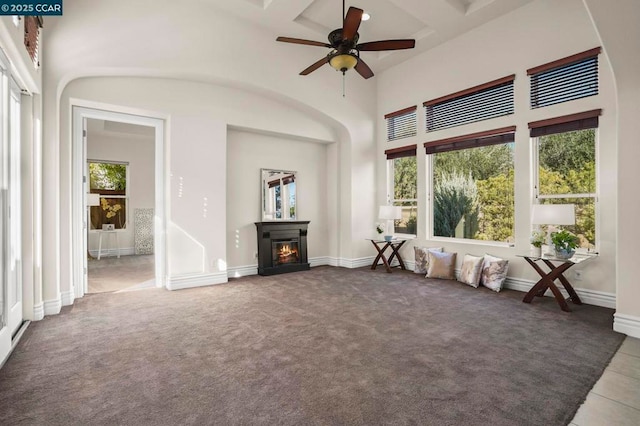 unfurnished living room with a high ceiling, beamed ceiling, ceiling fan, dark carpet, and coffered ceiling