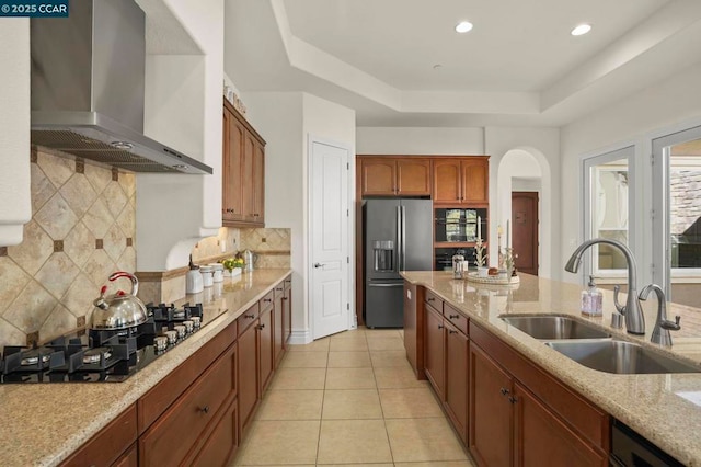 kitchen with wall chimney range hood, sink, black gas cooktop, stainless steel fridge with ice dispenser, and a raised ceiling