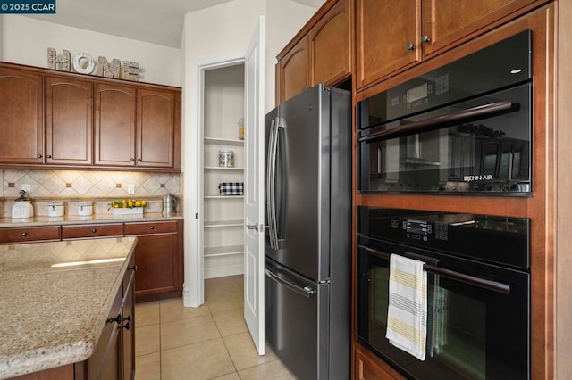 kitchen with light tile patterned floors, tasteful backsplash, light stone counters, and stainless steel refrigerator