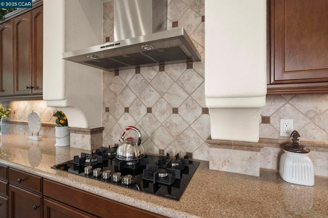 kitchen with tasteful backsplash, black gas cooktop, wall chimney exhaust hood, and light stone counters