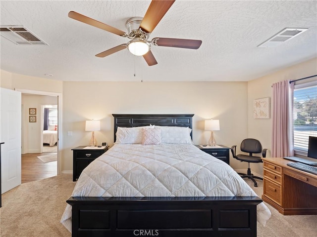 bedroom featuring a textured ceiling, light colored carpet, and ceiling fan