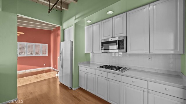 kitchen with stainless steel appliances, tasteful backsplash, white cabinets, and light wood-type flooring