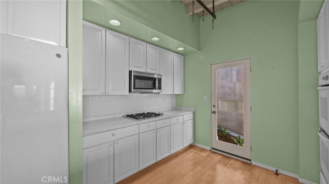 kitchen featuring appliances with stainless steel finishes, white cabinets, light hardwood / wood-style floors, and decorative backsplash