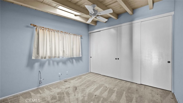 unfurnished bedroom with light carpet, wooden ceiling, a closet, beamed ceiling, and ceiling fan