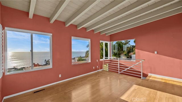 empty room with a water view, plenty of natural light, lofted ceiling with beams, and hardwood / wood-style floors