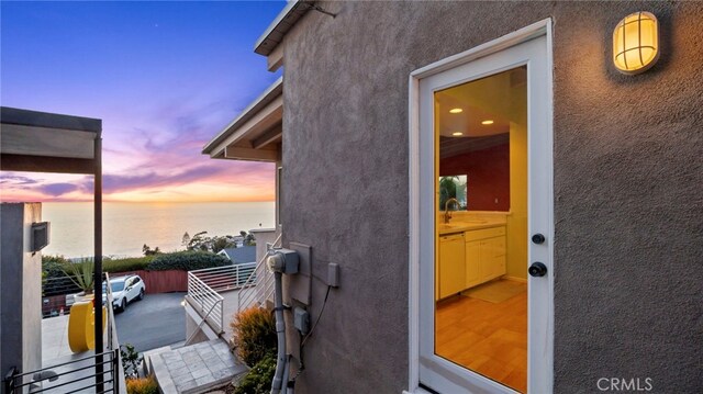 exterior entry at dusk featuring a water view, a balcony, and sink