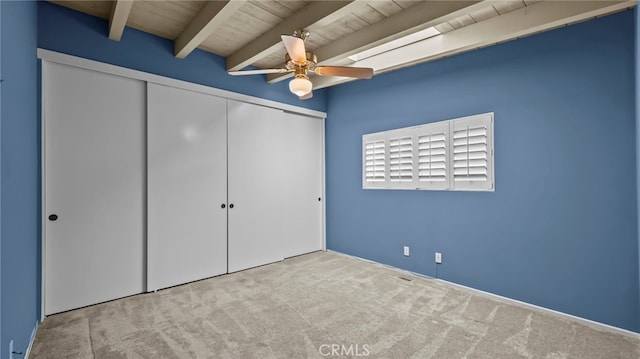 unfurnished bedroom featuring wood ceiling, ceiling fan, a closet, beamed ceiling, and light colored carpet