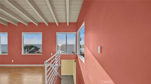 staircase featuring beamed ceiling, wood-type flooring, and a water view