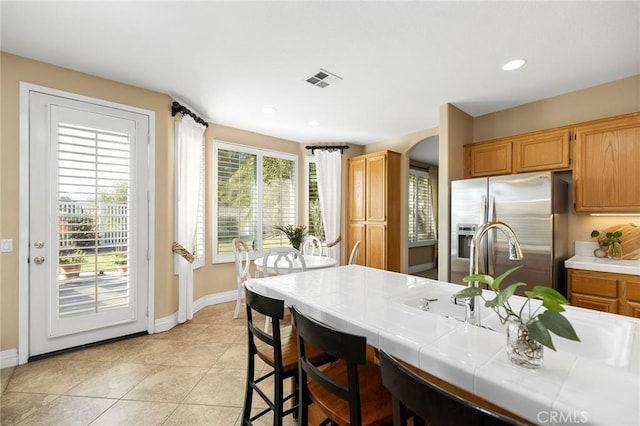 kitchen featuring tile counters, light tile patterned floors, a breakfast bar, and stainless steel fridge