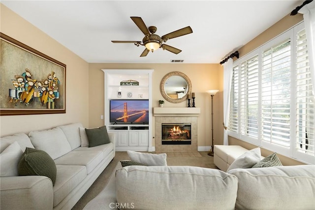 living room with ceiling fan, a tile fireplace, and built in shelves