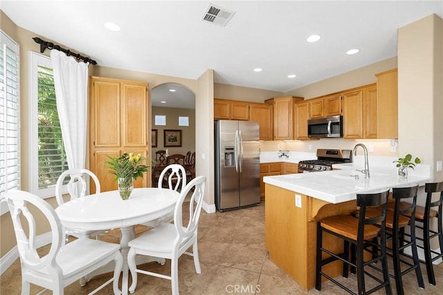 kitchen featuring kitchen peninsula, sink, light tile patterned flooring, appliances with stainless steel finishes, and a kitchen breakfast bar