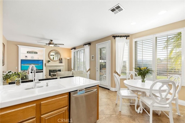 kitchen featuring ceiling fan, dishwasher, sink, light tile patterned flooring, and tile counters