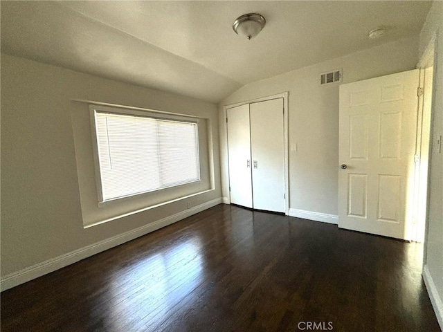 unfurnished bedroom featuring dark wood-type flooring, lofted ceiling, and a closet