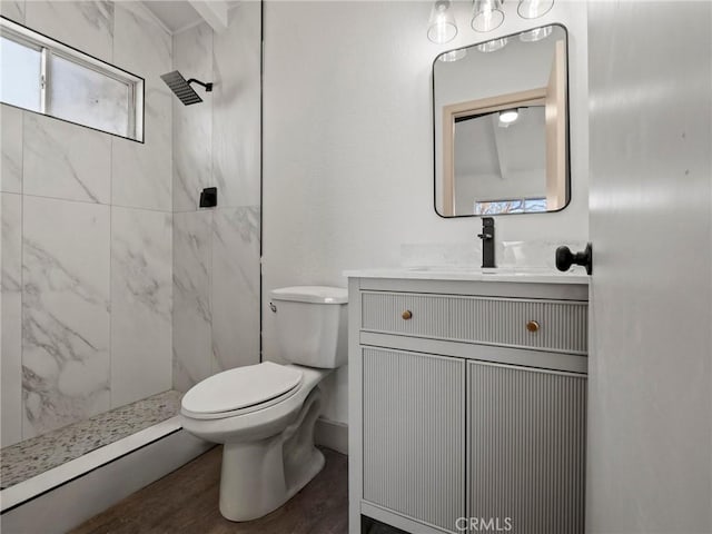 bathroom featuring toilet, tiled shower, wood-type flooring, and vanity