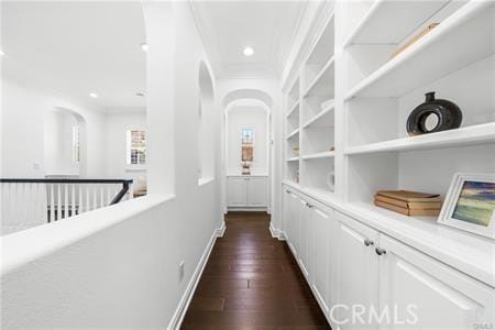 hall with dark wood-type flooring, built in features, and crown molding