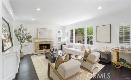 living room featuring dark hardwood / wood-style flooring, ornamental molding, and a stone fireplace