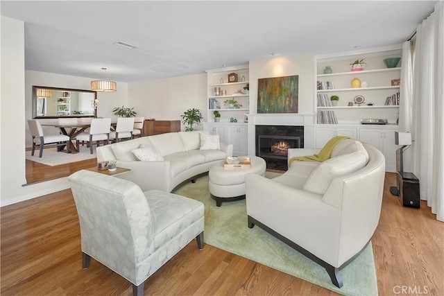 living room with built in features, a high end fireplace, and light hardwood / wood-style flooring