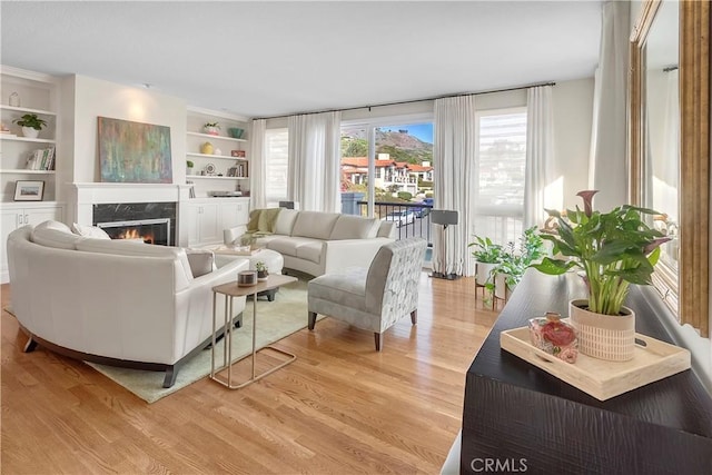 living room with a premium fireplace, plenty of natural light, light hardwood / wood-style flooring, and built in shelves