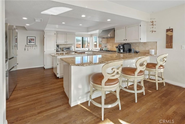 kitchen with appliances with stainless steel finishes, wall chimney exhaust hood, a tray ceiling, and white cabinets