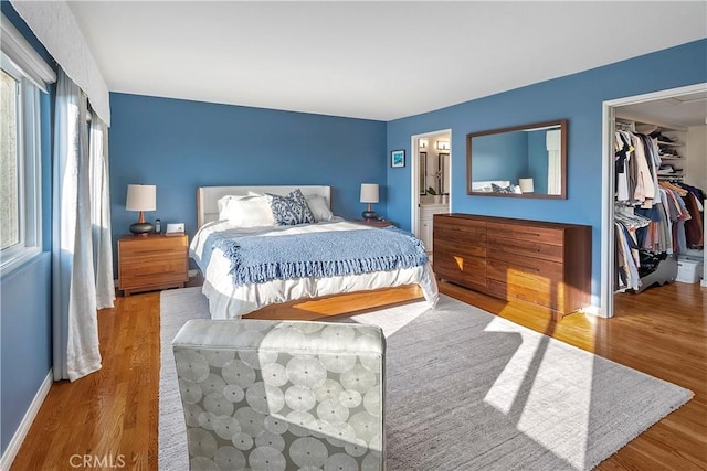 bedroom with light wood-type flooring, a spacious closet, ensuite bath, and a closet