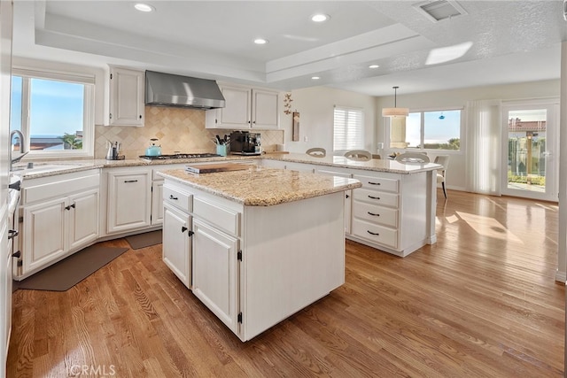 kitchen featuring hanging light fixtures, a center island, white cabinets, and wall chimney exhaust hood