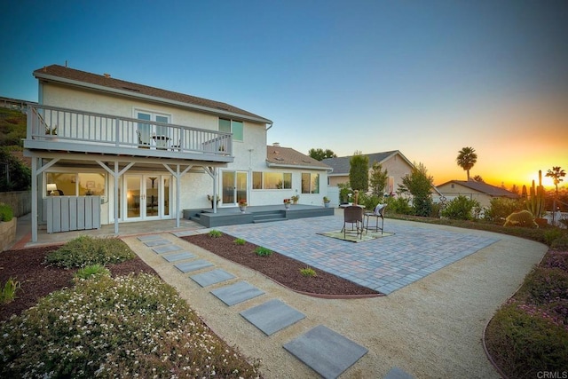 back house at dusk featuring french doors, a patio area, and a balcony