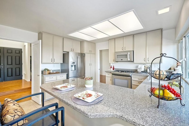 kitchen with kitchen peninsula, a kitchen bar, light tile patterned flooring, stainless steel appliances, and light stone counters