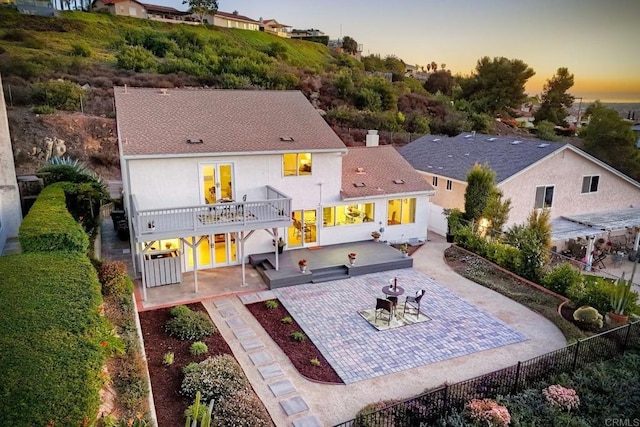 back house at dusk with a balcony and a patio