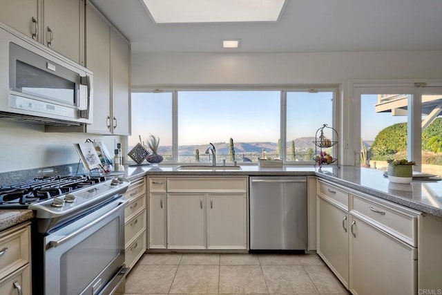 kitchen featuring light tile patterned floors, a mountain view, appliances with stainless steel finishes, light stone countertops, and sink